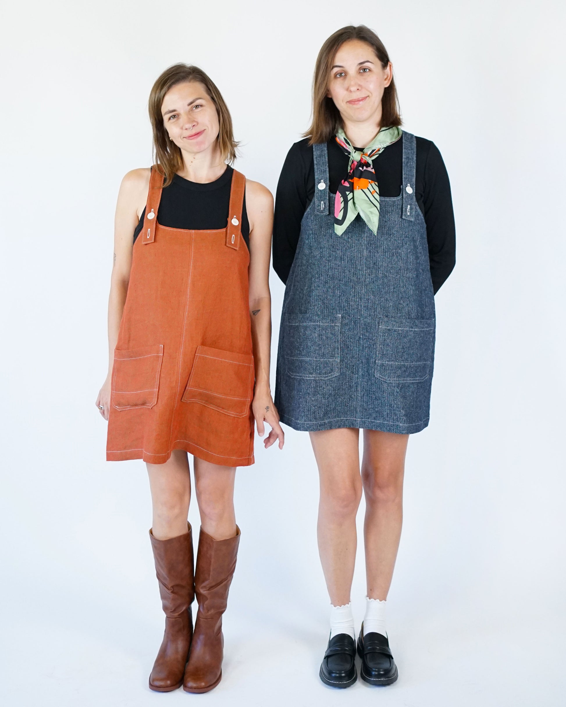 Two women wearing different colored overalls against a white background