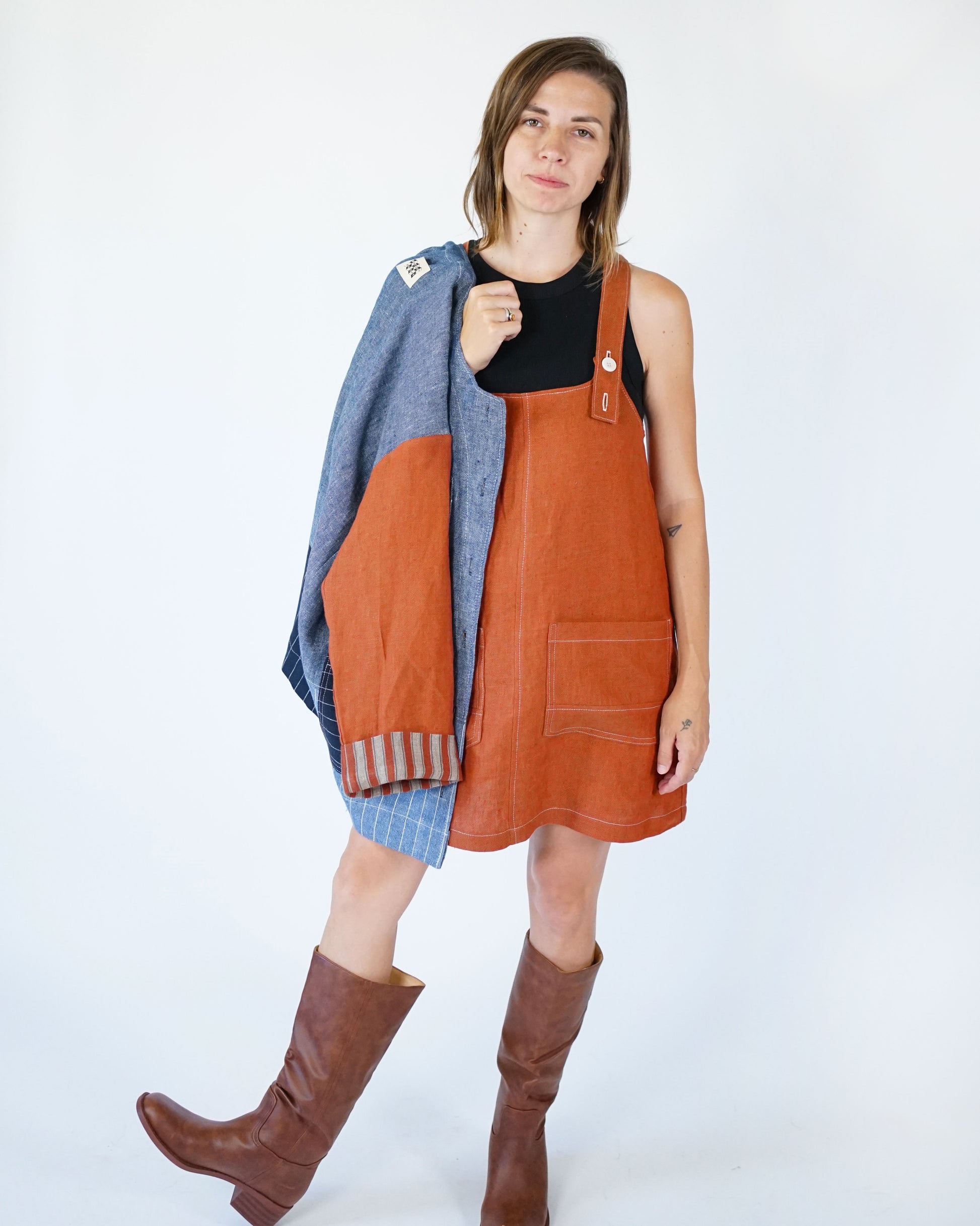 Woman wearing a brown overalls dress with a blue cardigan on a white background