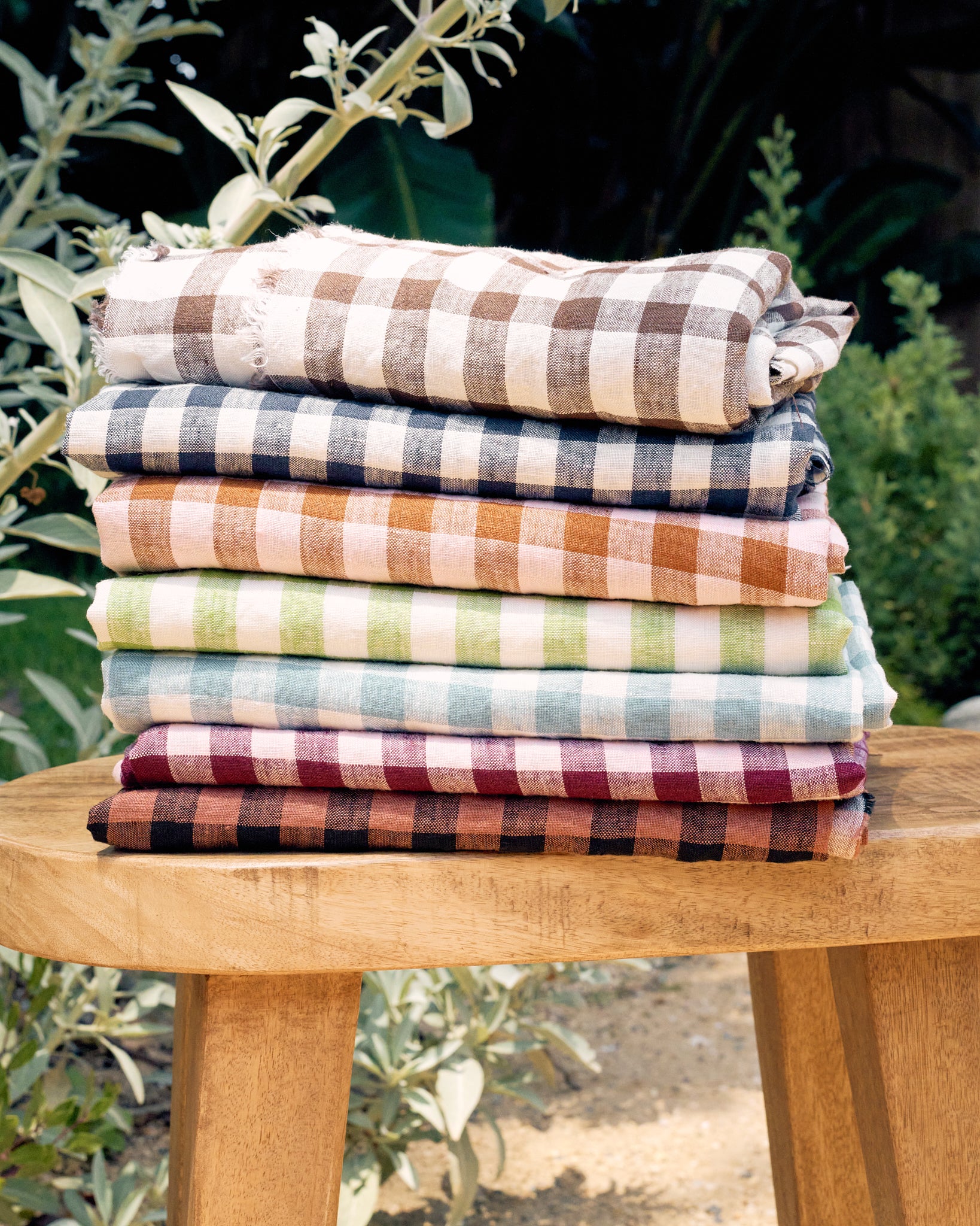 Stack of gingham linen fabrics on a wooden stool with a natural outdoor background