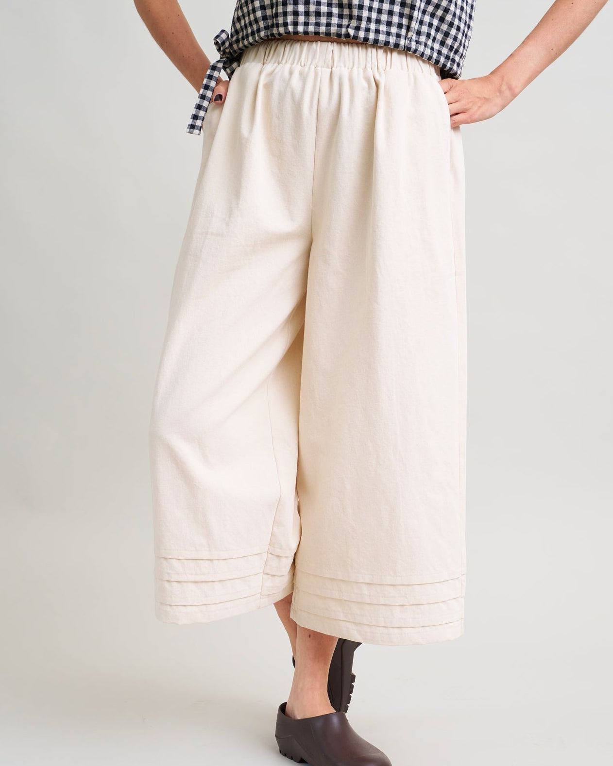 Person wearing a checkered top and beige wide-leg pants on a white background