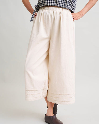 Person wearing a checkered top and beige wide-leg pants on a white background