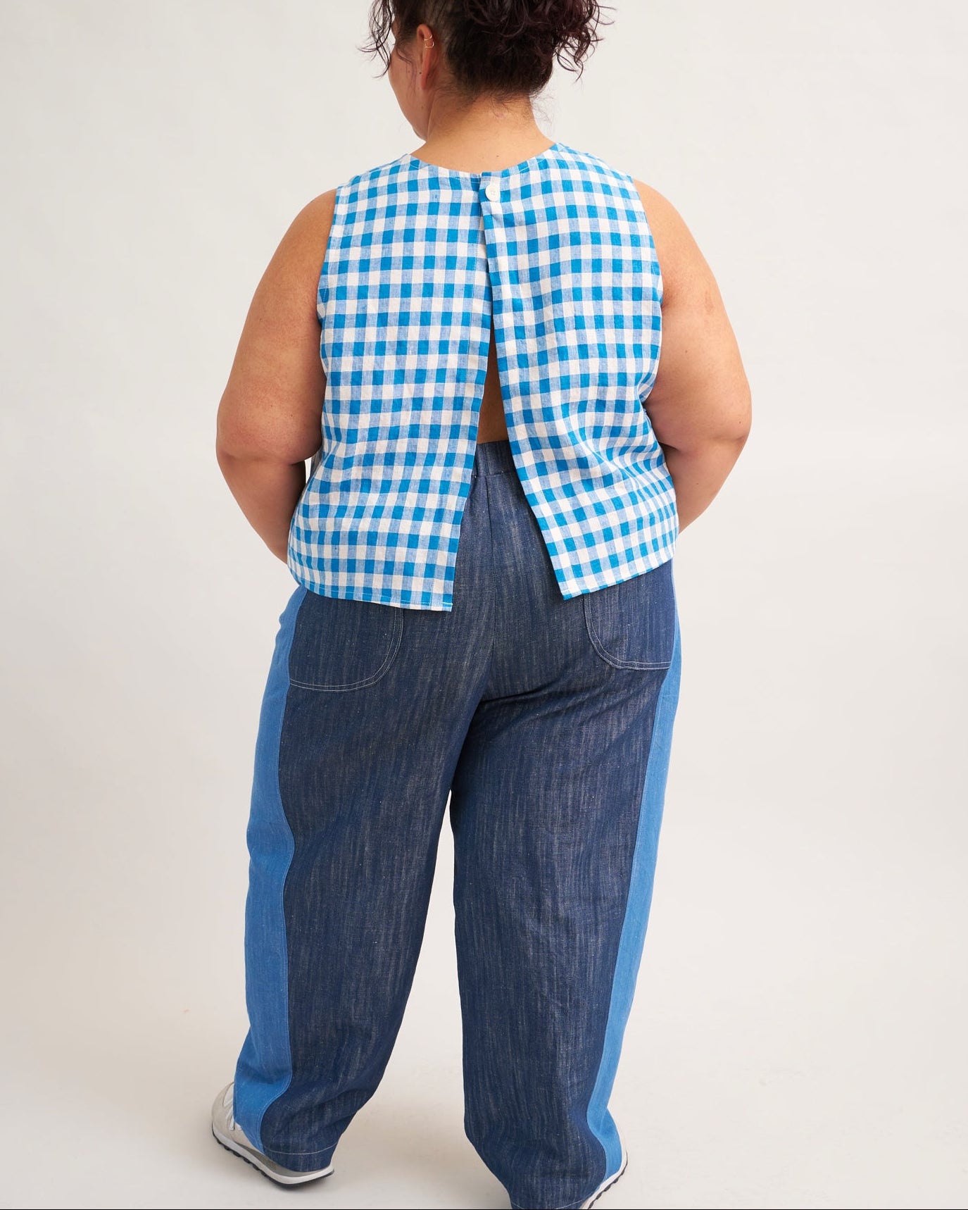 Person wearing a blue and white checkered top and blue pants on a plain background