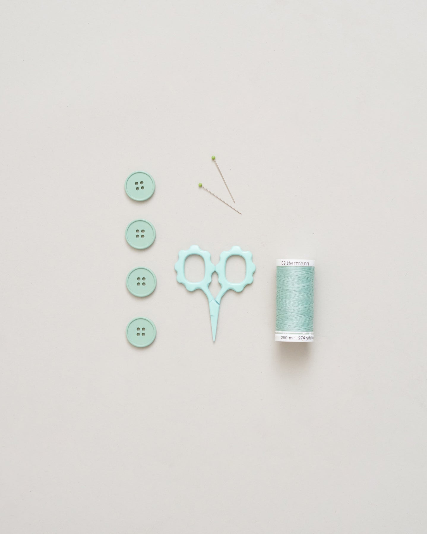Mint green buttons, scissors, and spool of thread on a light gray background