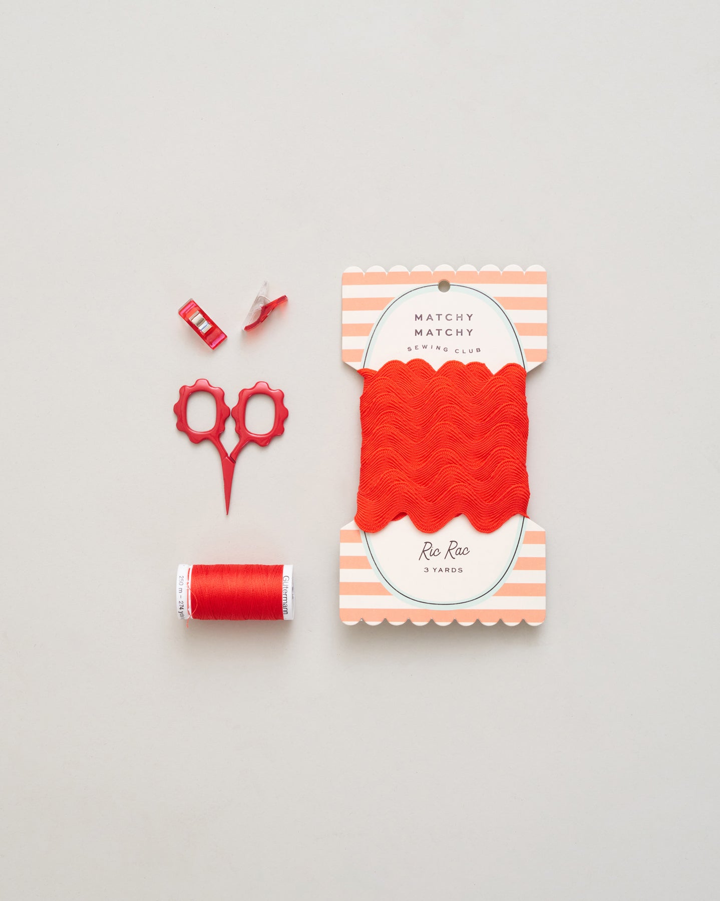 Red thread spool, scissors, and packaging on a light gray background