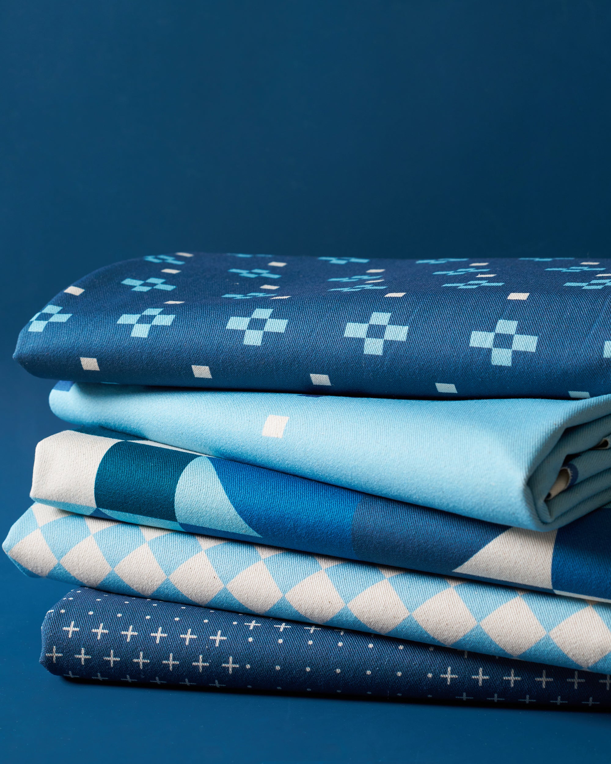 Stack of blue fabric swatches with various patterns on a dark blue background
