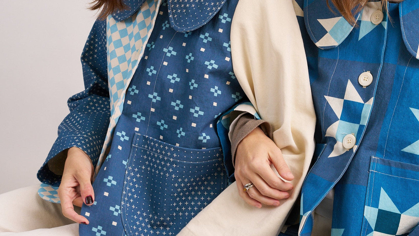Two women wearing blue patterned jackets sitting together on a white background