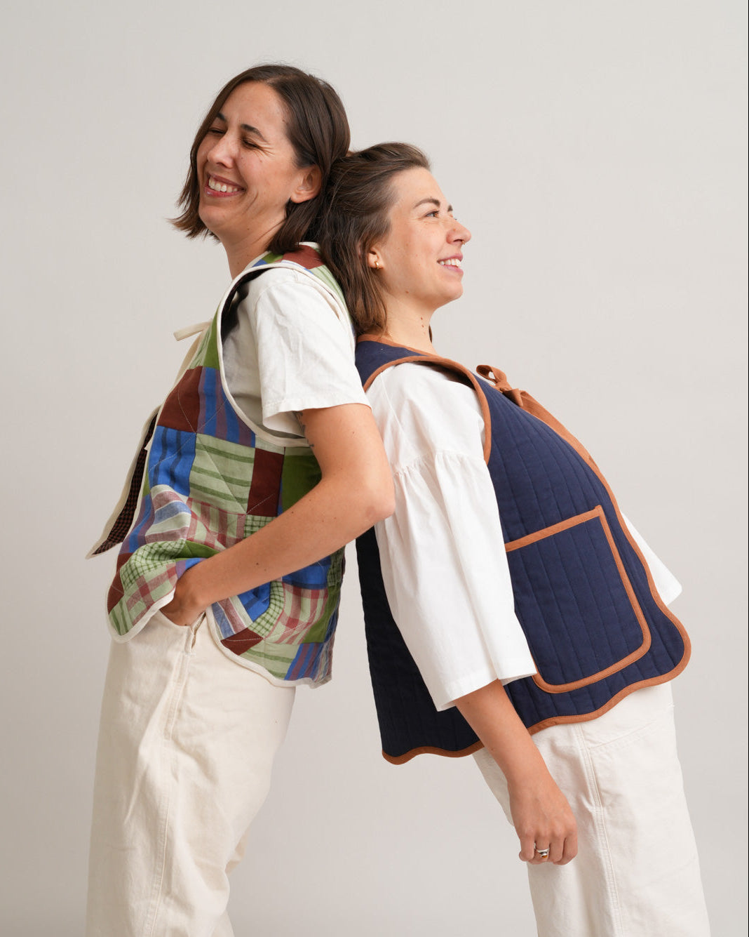 Two women wearing colorful vests against a plain background
