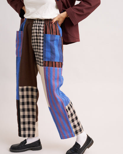 Person wearing patchwork pants with blue, brown, and plaid patterns on a white background
