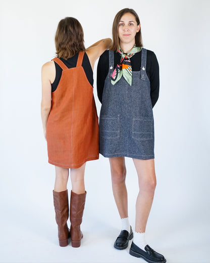 Two women wearing denim overalls against a white background