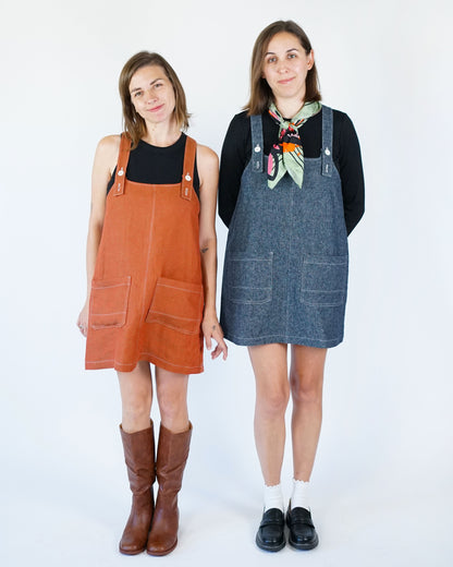Two women wearing different colored overalls against a white background
