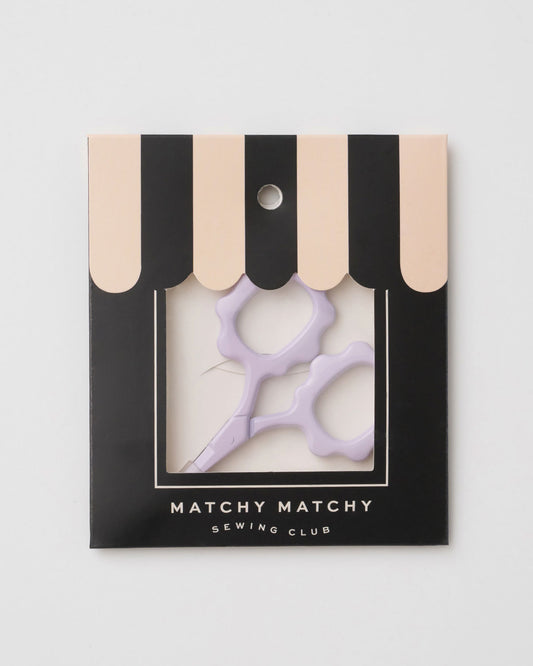 Purple scissors in a black and beige striped box with 'Matchy Matchy Sewing Club' branding on a light gray background.